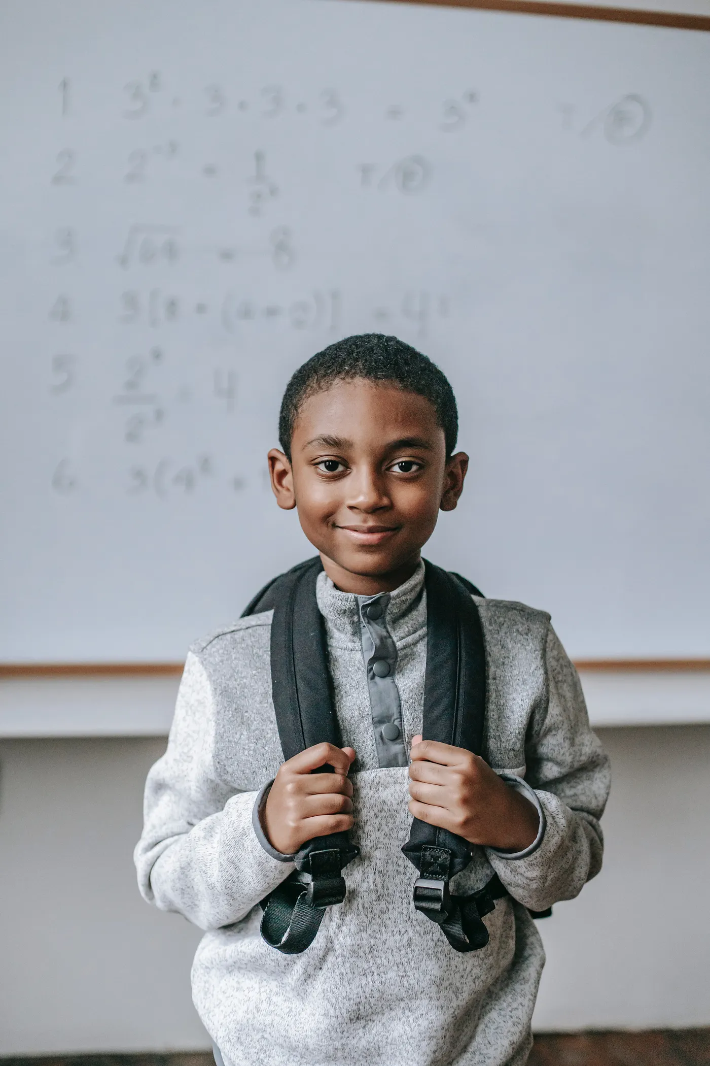 a boy in a classroom holding a bag-pack
